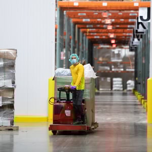 A team member safely drives an electric palette straddle stacker